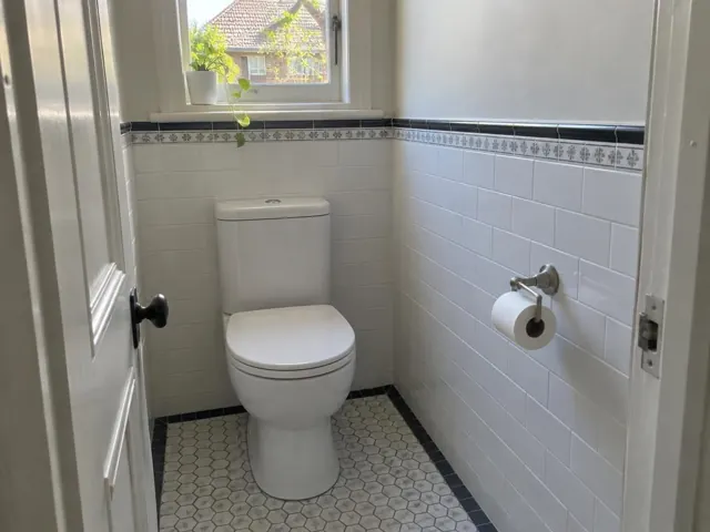 Clean white toilet in a tiled bathroom with a window and patterned floor in Botany