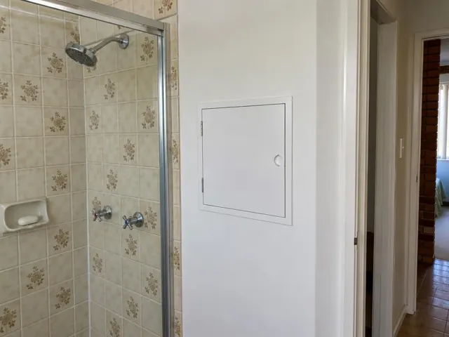 Small access panel in a painted bathroom wall beside a tiled shower in Pagewood